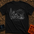Running In The Background - T-Shirt in Black - A line-art illustration of a man wearing a beanie sitting in a camp chair...