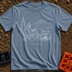 Running In The Background - T-Shirt in Blue Jean - A line-art illustration of a man wearing a beanie sitting in a camp...