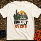 Bigfoot Believes In Us - T-Shirt in Ivory - A graphic showing a silhouette of Bigfoot peeking from behind a large pine...