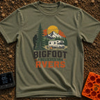 Bigfoot Believes In Us - T-Shirt in Moss - A graphic showing a silhouette of Bigfoot peeking from behind a large pine...