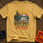 Bigfoot Believes In Us - T-Shirt in Mustard - A graphic showing a silhouette of Bigfoot peeking from behind a large pine...