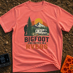 Bigfoot Believes In Us - T-Shirt in Watermelon - A graphic showing a silhouette of Bigfoot peeking from behind a large...