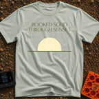 Booked Till Sunset - T-Shirt in Bay - The image features the text "BOOKED SOLID THROUGH SUNSET" in a dark olive green,...