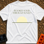 Booked Till Sunset - T-Shirt in White - The image features the text "BOOKED SOLID THROUGH SUNSET" in a dark olive green,...