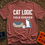 Cat Logic Certified - T-Shirt in Brick - A black and white cat sitting upright next to an empty round pet bed, with a...