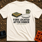Fork Found Too Late - T-Shirt in Ivory - A cartoon illustration showing a fork partially hidden under a folded green...