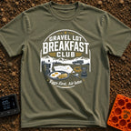 Gravel Gourmet Gathering - T-Shirt in Moss - A camping breakfast setup featuring a Moka pot, a pan of eggs and bacon, a...