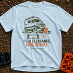 High Clearance Low Drama - T-Shirt in Chambray - A lifted camper van is shown driving over rocks next to two orange...