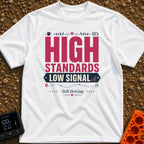 Standards And Signals - T-Shirt in White - A typographic design reading "HIGH STANDARDS LOW SIGNAL" and "Still thriving",...