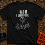 It Was Just Here - T-Shirt in Black - A white line drawing of a person in a beanie and jacket looking down and searching...