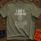 It Was Just Here - T-Shirt in Moss - A white line drawing of a person in a beanie and jacket looking down and searching...