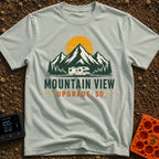 Peak View Upgrade - T-Shirt in Bay - A graphical illustration of a Class C motorhome parked in front of a pine forest and...