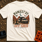 Namastay Off Grid - T-Shirt in Ivory - A person is sitting cross-legged on a yoga mat beside a steaming mug of coffee,...