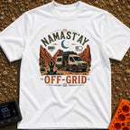 Namastay Off Grid - T-Shirt in White - A person is sitting cross-legged on a yoga mat beside a steaming mug of coffee,...