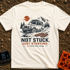 Not Stuck Just Studying - T-Shirt in Ivory - An illustration of a muddy 4x4 SUV stopped on a rugged trail, with an open...