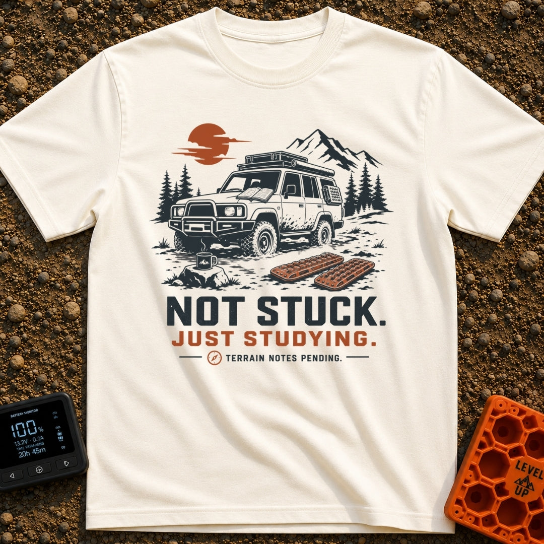 Not Stuck Just Studying - T-Shirt in Ivory - An illustration of a muddy 4x4 SUV stopped on a rugged trail, with an open...