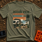 Ocean View Loading - T-Shirt in Moss - A camper van is parked by the ocean at sunset with a roof-mounted solar panel and...
