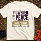 Peaceful Paw Power - T-Shirt in Ivory - A typographic design featuring the phrases "POWERED BY PEACE AND PAW PRINTS" and...