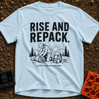 Rise And Repack - T-Shirt in Chambray - A black-and-white illustration of a man kneeling to roll up a sleeping bag, with...