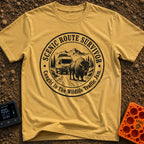 Survived The Scenic Route - T-Shirt in Mustard - A circular, black-and-white illustration of a camper van stopped on a...