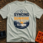 Rise And Sync - T-Shirt in Bay - A circular badge design featuring a white camper van parked by a lake with mountains and...