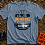 Rise And Sync - T-Shirt in Blue Jean - A circular badge design featuring a white camper van parked by a lake with...