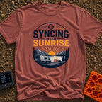 Rise And Sync - T-Shirt in Brick - A circular badge design featuring a white camper van parked by a lake with mountains...