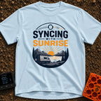 Rise And Sync - T-Shirt in Chambray - A circular badge design featuring a white camper van parked by a lake with...