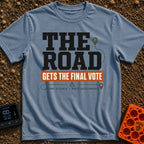 The Road Votes Last - T-Shirt in Blue Jean - A typographic design featuring the large text "THE ROAD" above a brown...