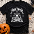 The Solar Seance - T-Shirt in Black - A vintage-style white line drawing of a hooded figure holding up foldable solar...