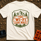 Mountains Over Modems - T-Shirt in Ivory - A badge-shaped graphic featuring green mountains, pine trees, and a winding...