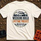 Lifetime Weekend Build - T-Shirt in Ivory - A circular graphic showing a white camper van parked near pine trees and...
